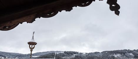 Tejado nevado con estructura de madera tradicional y una torre a lo lejos.