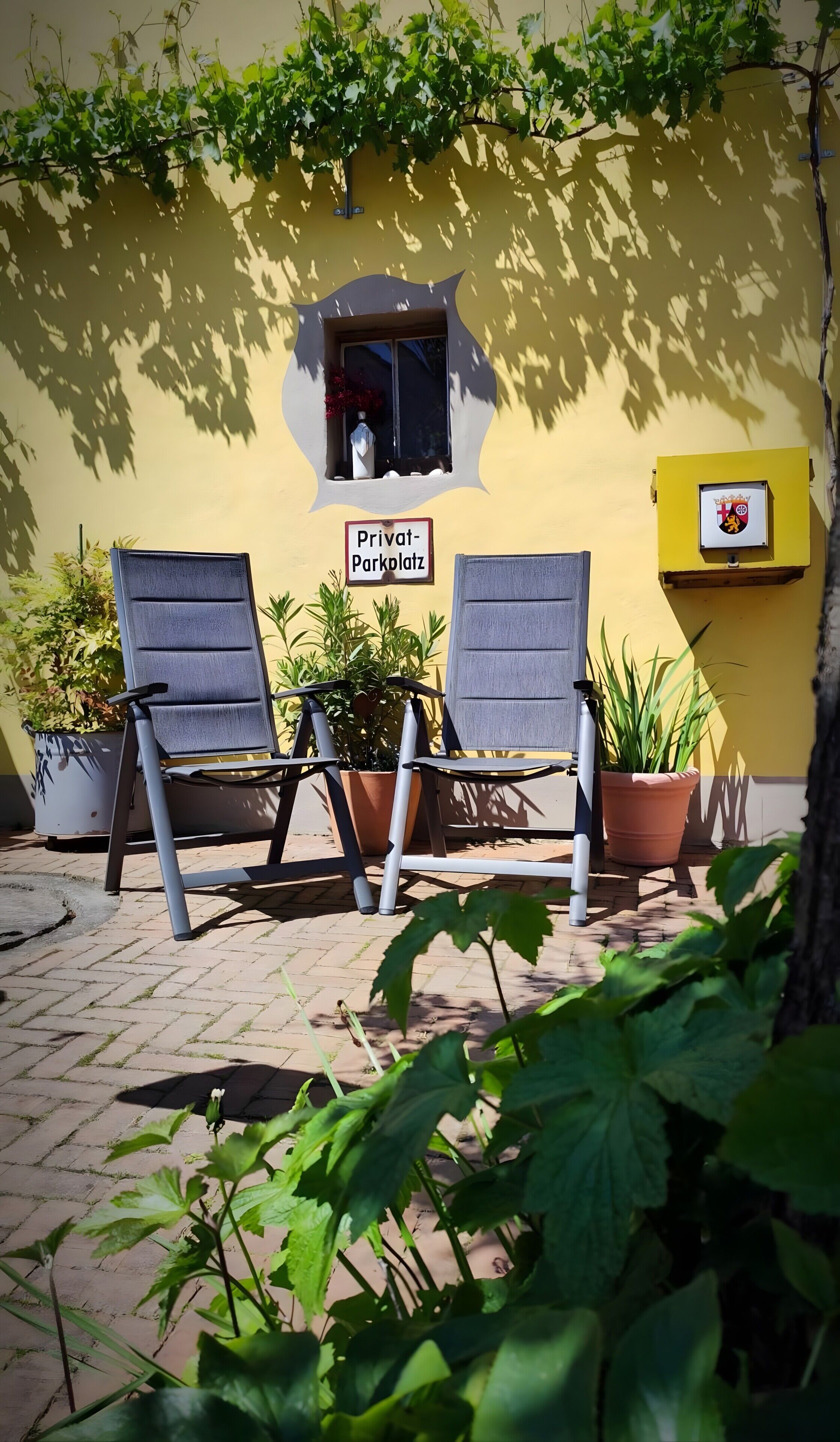 Deux chaises sont placées à l’extérieur d’un bâtiment. On peut y voir une pancarte indiquant « Parking privé » et un blason sur le mur.