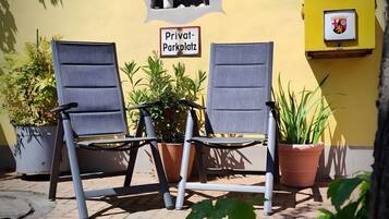 Deux chaises sont placées à l’extérieur d’un bâtiment. On peut y voir une pancarte indiquant « Parking privé » et un blason sur le mur.