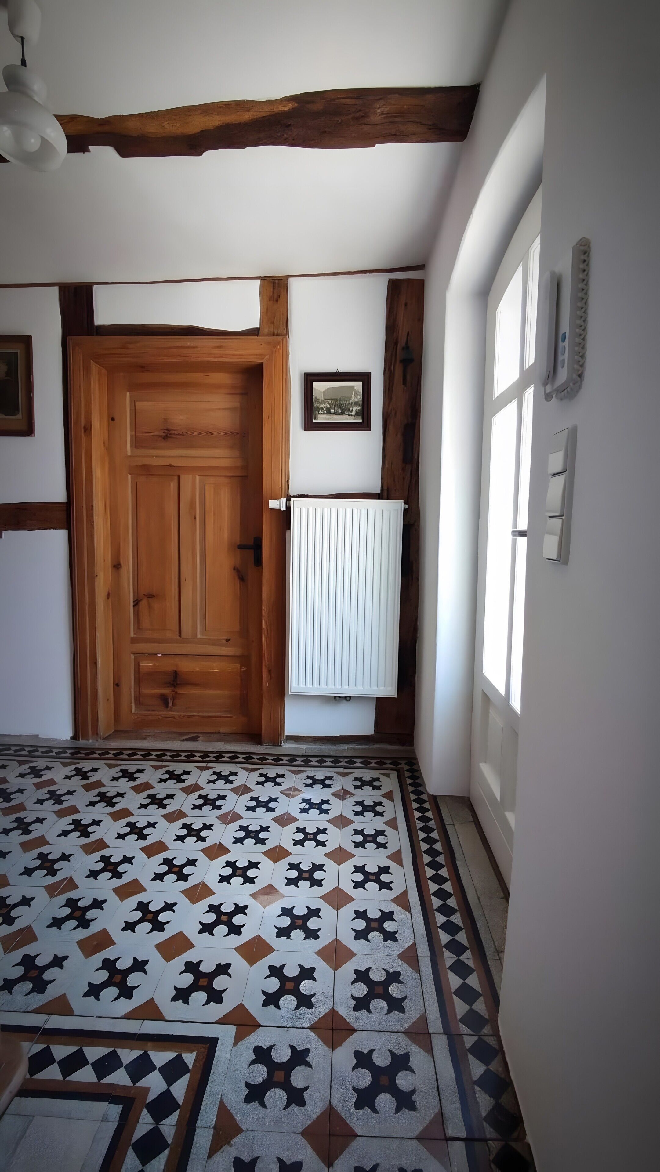 Un pasillo con una puerta de madera, un radiador y baldosas de suelo con diseño.