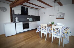 A compact kitchen with white cabinets, a refrigerator, an oven, and a dining table with chairs. - Apartment 'La Maison Palatinate' with Charm, Southern Wine Route (Kapsweyer)