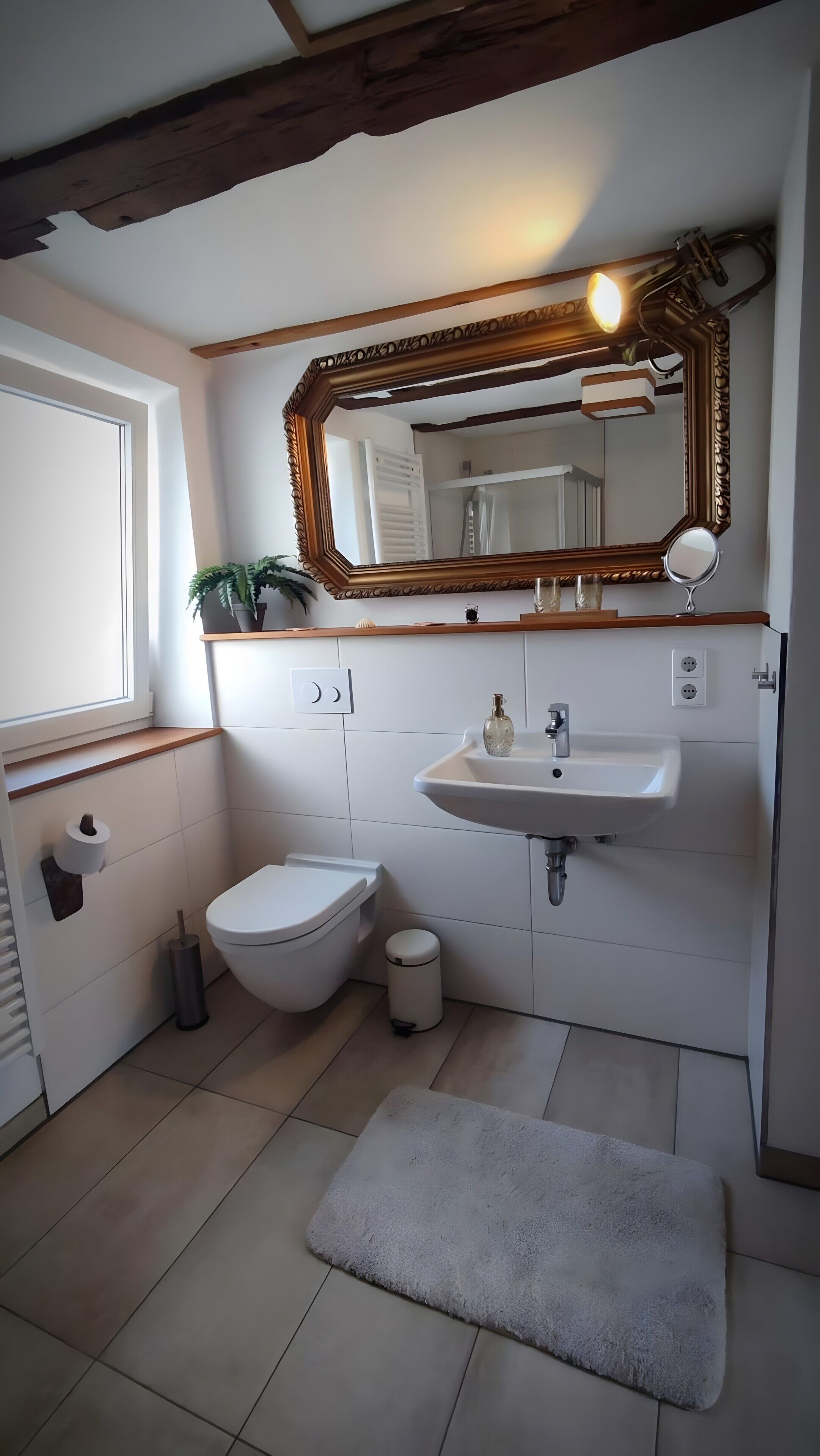 Ein Badezimmer mit Toilette, Waschbecken, Spiegel und einem kleinen Mülleimer.