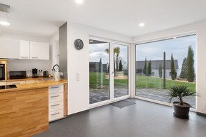 A modern kitchen with a wooden countertop, white cabinets, and a large sliding glass door leading to a patio. - Holiday Apartment 'Relax Oasis' with Mountain View, Private Terrace & Wi-Fi (Sasbachwalden)