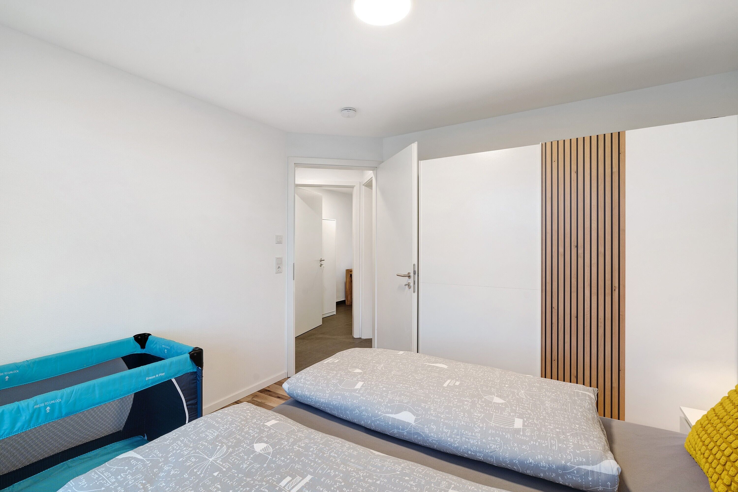 Un dormitorio con dos camas, un panel de pared de listones de madera y un pasillo que lleva a otra habitación.