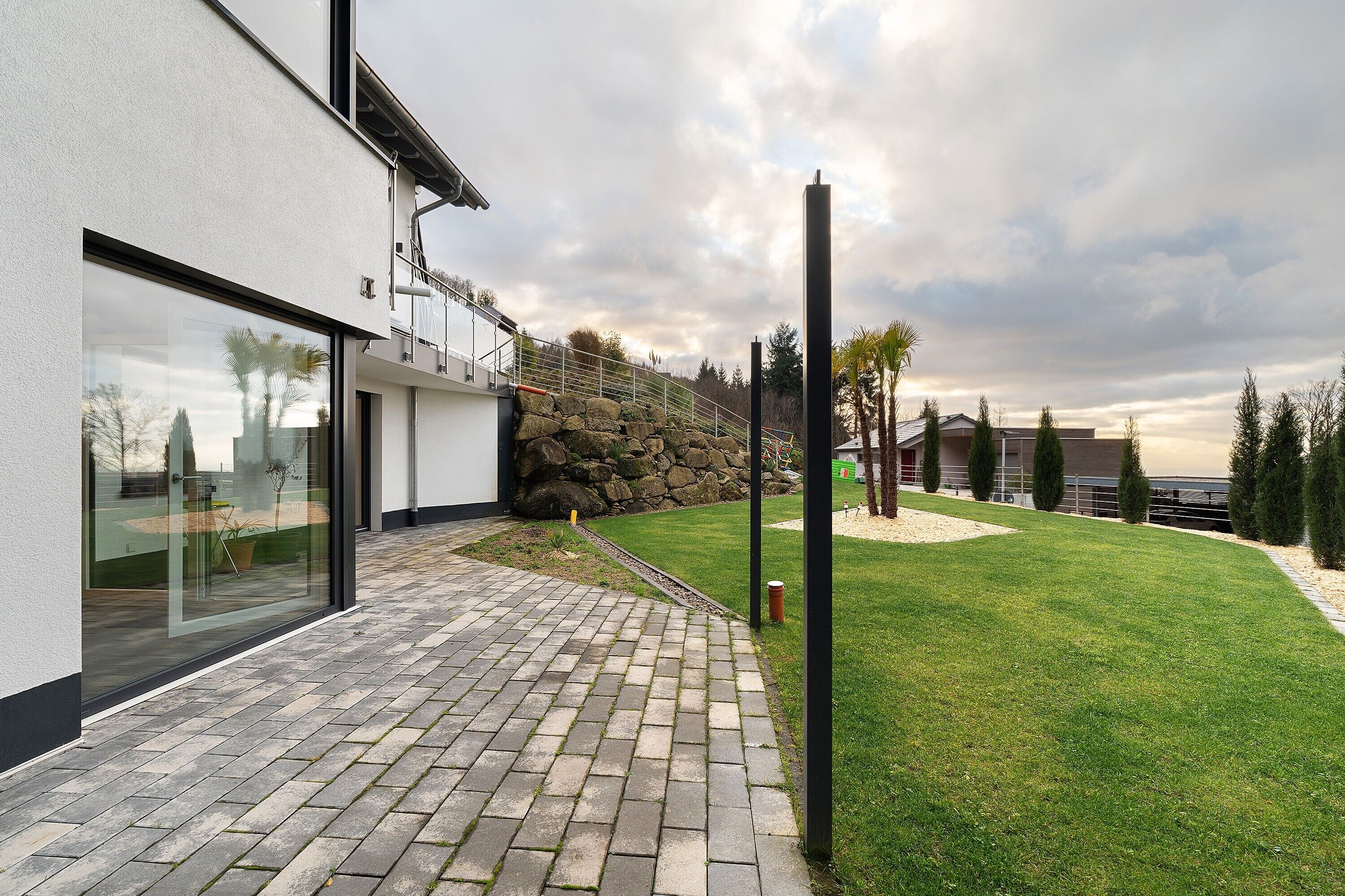 A modern building with a paved walkway, a stone wall, and a well-maintained lawn.