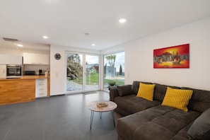 A modern living room with a sofa, a coffee table, and a kitchen area with cabinets and appliances. - Holiday Apartment 'Relax Oasis' with Mountain View, Private Terrace & Wi-Fi (Sasbachwalden)