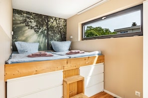 Un dormitorio con una cama litera, una ventana con vistas, un mural en la pared y un pequeño armario de madera.