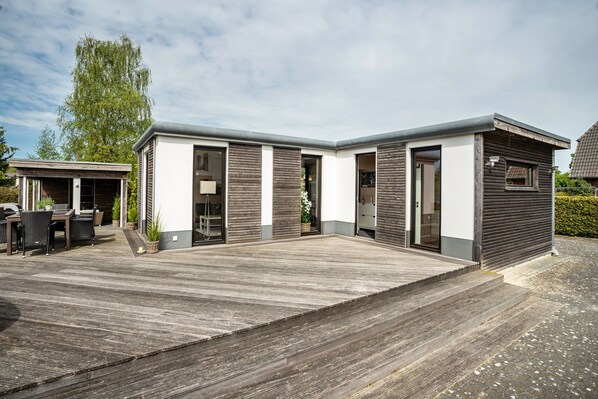 A modern two-story building with a flat roof, large windows, and a covered outdoor area with a wooden deck. - Holiday Home 'Nova Ferienhaus, 50qm' with Private Terrace, Private Garden and Wi-Fi (Ueckermünde)