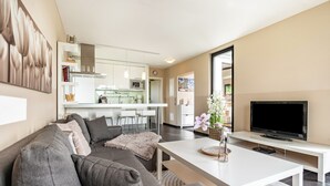 Un salon moderne avec un canapé gris, un téléviseur à écran plat et une cuisine en arrière-plan.