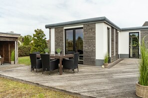 A modern house with a patio, outdoor furniture, and a large sliding glass door. - Holiday Home 'Nova Ferienhaus, 50qm' with Private Terrace, Private Garden and Wi-Fi (Ueckermünde)