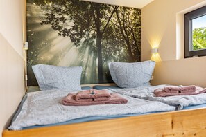 A double bed with two pillows, a wall-mounted artwork of a forest, and a window with daylight. - Holiday Home 'Nova Ferienhaus, 50qm' with Private Terrace, Private Garden and Wi-Fi (Ueckermünde)