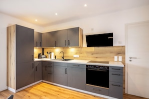 Een moderne keuken met grijze kastjes, een ingebouwde oven en een flatscreen televisie boven de aanrecht.