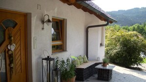 Una casa con ingresso in pietra, una porta in legno, una finestra con stipite in legno, un lampadario a parete e una pianta in vaso.