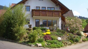 Una casa a due piani con un balcone, circondata da un giardino pieno di piante e fiori.