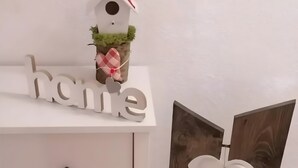 Un comò bianco con cassetti, una scultura in legno a forma di cuore e una casetta per uccelli con un fiore rosso.