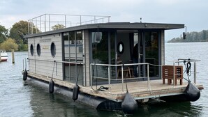 Ein Hausboot mit einer überdachten Terrasse, einem Essbereich und einem Badezimmer.