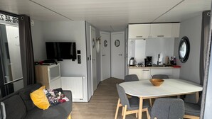 Ein kompakter Wohnbereich mit einer Couch, einem Esstisch mit Stühlen, einer Küchenzeile, einem Fernseher und einem Spiegel.