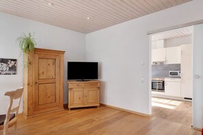 Une pièce comprenant un meuble en bois, une télévision, une chaise et donnant sur un coin cuisine.