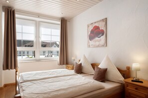 Une chambre d’hôtel avec un lit, deux tables de chevet, une fenêtre avec des rideaux et un tableau accroché au mur.