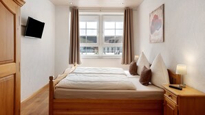 Une chambre d’hôtel avec un lit, une télévision, une fenêtre avec des rideaux, une lampe et un tableau au mur.