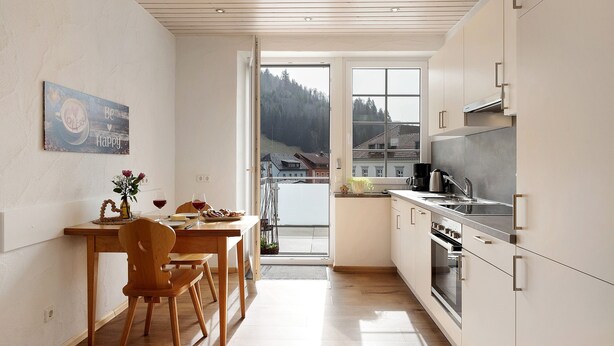 Une cuisine moderne avec des meubles en bois, un coin repas avec une table et des chaises en bois, et une grande fenêtre donnant sur une zone boisée.