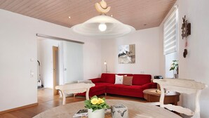 Un salon moderne avec un canapé rouge, des meubles en bois, une table ronde ornée d’un vase de fleurs et un ventilateur de plafond.