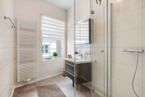 Een moderne badkamer met een douchecabine van glas, een witte radiator en een raam met zonwering.