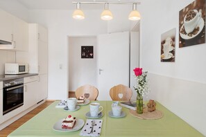 Una cocina moderna con armarios blancos, un microondas y una mesa de comedor con platos, tazas y un jarrón con flores.
