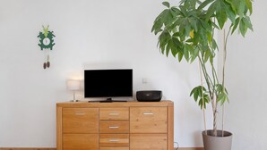 A wooden cabinet with drawers, a television, a speaker, and a potted plant against a white wall.