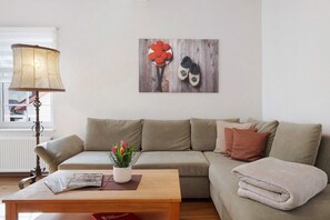 Una sala de estar con sofá, mesa de centro, lámpara, un cuadro en la pared y ventana.