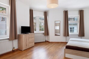 A bedroom with a bed, a TV on a wooden dresser, a radiator, and windows with curtains. - Apartment 'Ferienwohnung Silberbergblick' with Wi-Fi (Todtnau)