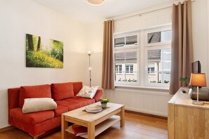 A modern living room with a red sofa, a wooden coffee table, a floor lamp, and a window with curtains.