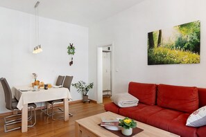 A modern living room with a dining table, red sofa, and a painting of a forest. - Apartment 'Ferienwohnung Silberbergblick' with Wi-Fi (Todtnau)