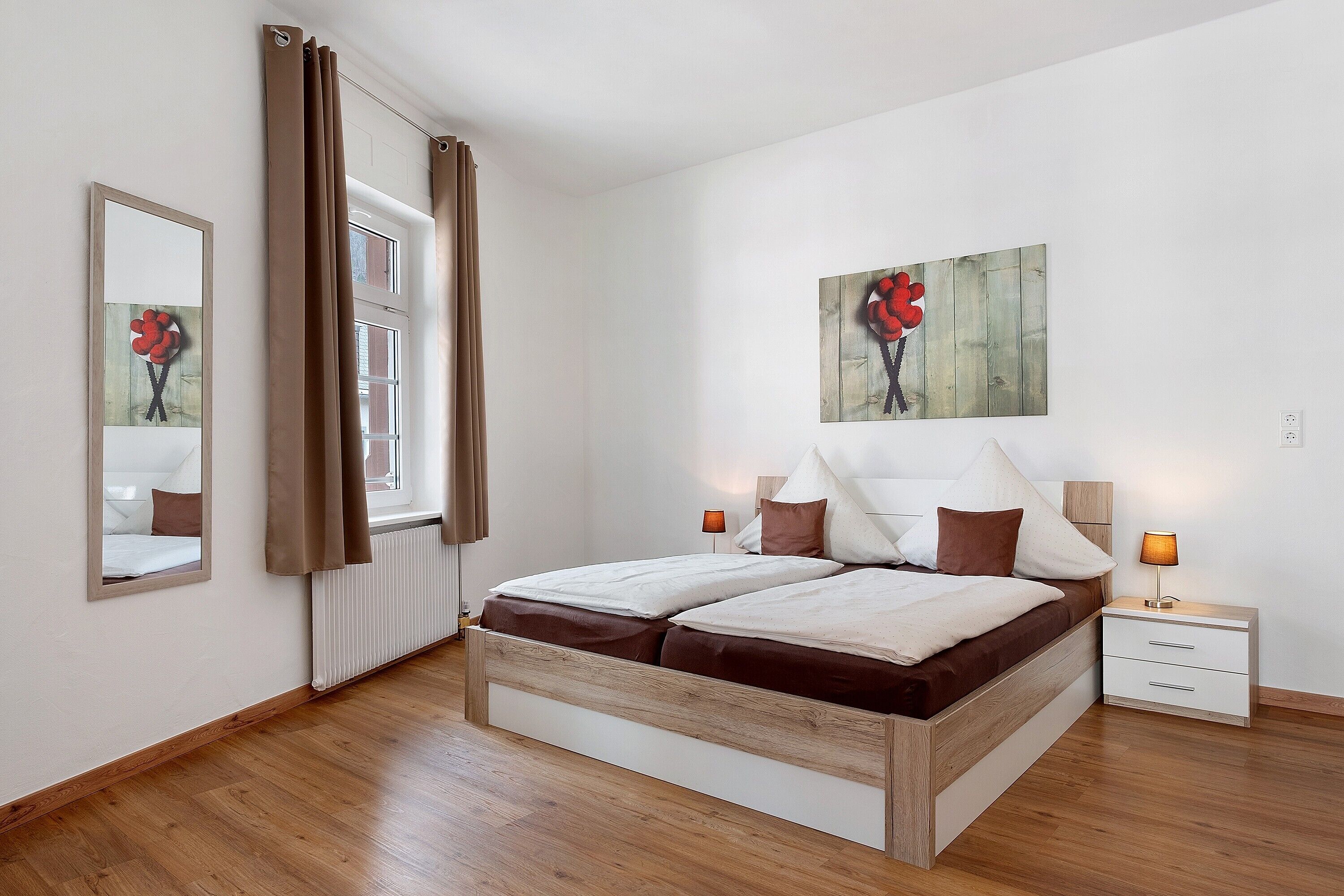 A bedroom with a wooden bed, a nightstand, a mirror, and a window with curtains.