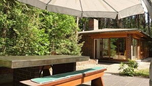 Ein Außenbereich mit Sitzgelegenheit, Tisch und Bank, einem großen Sonnenschirm und einem Gebäude mit Glastüren.