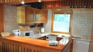 Eine kleine Küche mit Holzschränken, einer eingebauten Mikrowelle, einem Spülbecken und einem Fenster.