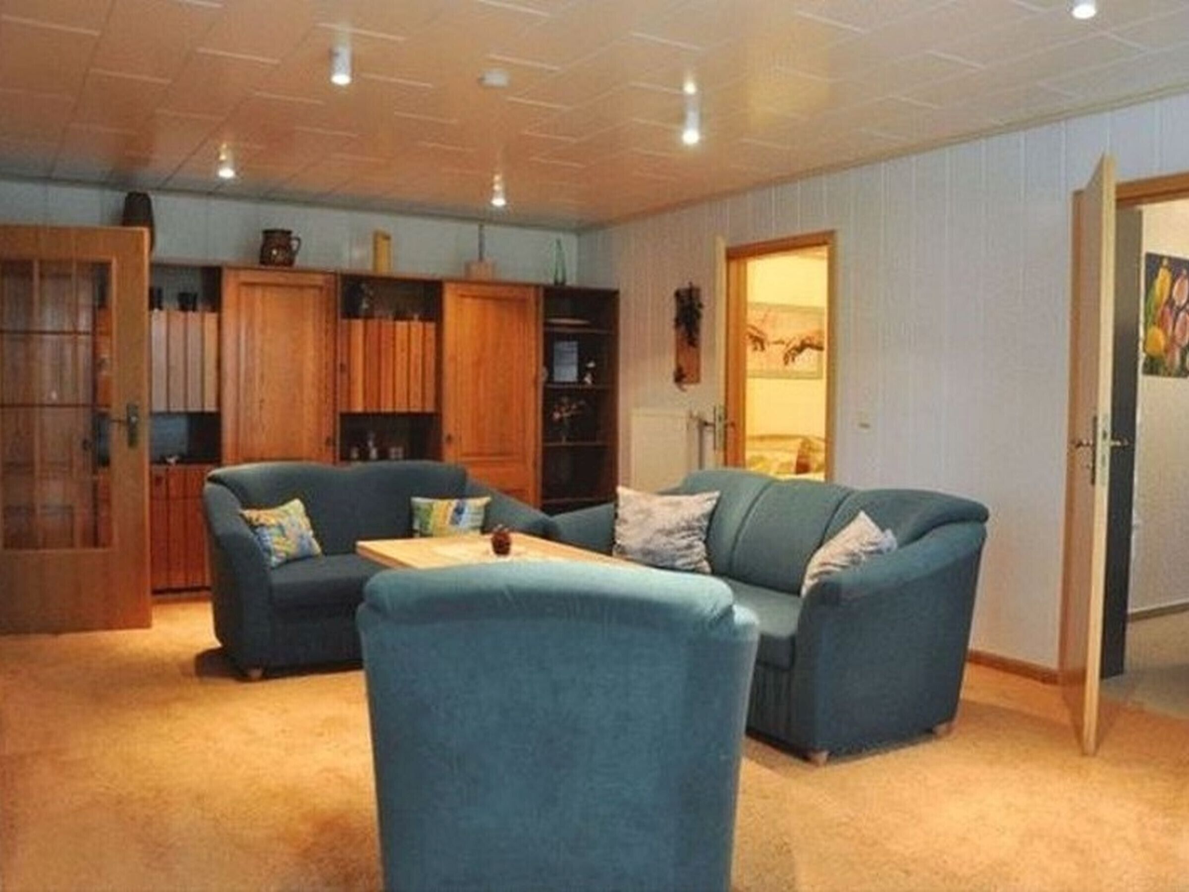 Ein Wohnzimmer mit einem blauen Sofagarnitur, Holzkredänzen und einem Teppichboden.