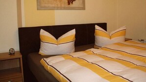 Ein Bett mit gestreifter Bettwäsche, ein Nachttisch mit einer Uhr und ein Wandbild mit Händen.