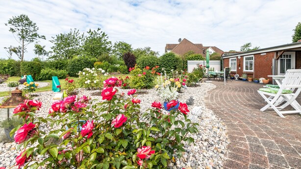 Ein Garten mit Pflasterterrasse, Gartenmöbeln und einem Ziegelgebäude im Hintergrund.