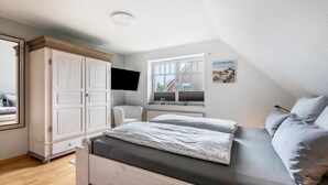 A bedroom with a bed, a wardrobe, a TV, a window, and a chair.