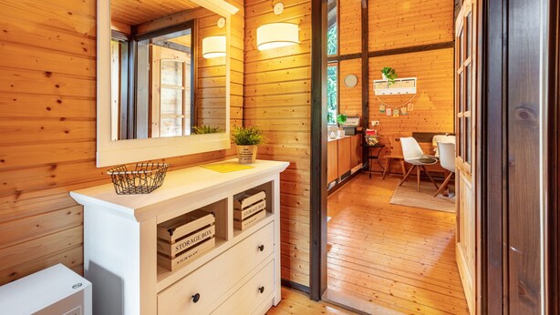 Ein Holzinterieur mit einem weißen Schminktisch, Aufbewahrungsboxen, einem Spiegel und Blick in einen Essbereich.