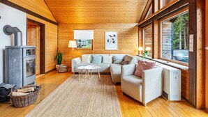 Ein gemütliches Blockhaushaus-Interieur mit Holzbalkendecke, einer Couch, einem kleinen Tisch und einem Kamin.