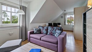Een moderne woonkamer met een paarse bank, een eethoek en een keuken die door een open deur zichtbaar is.