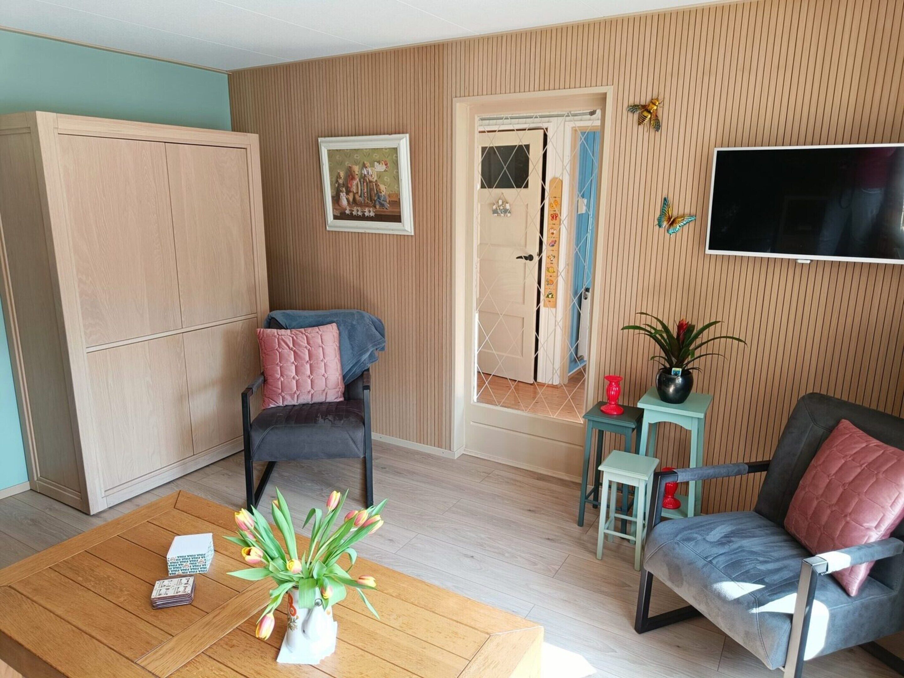 A living room with a wooden floor, a sofa, a chair, a coffee table with a vase of flowers, a television, and a door with a window.