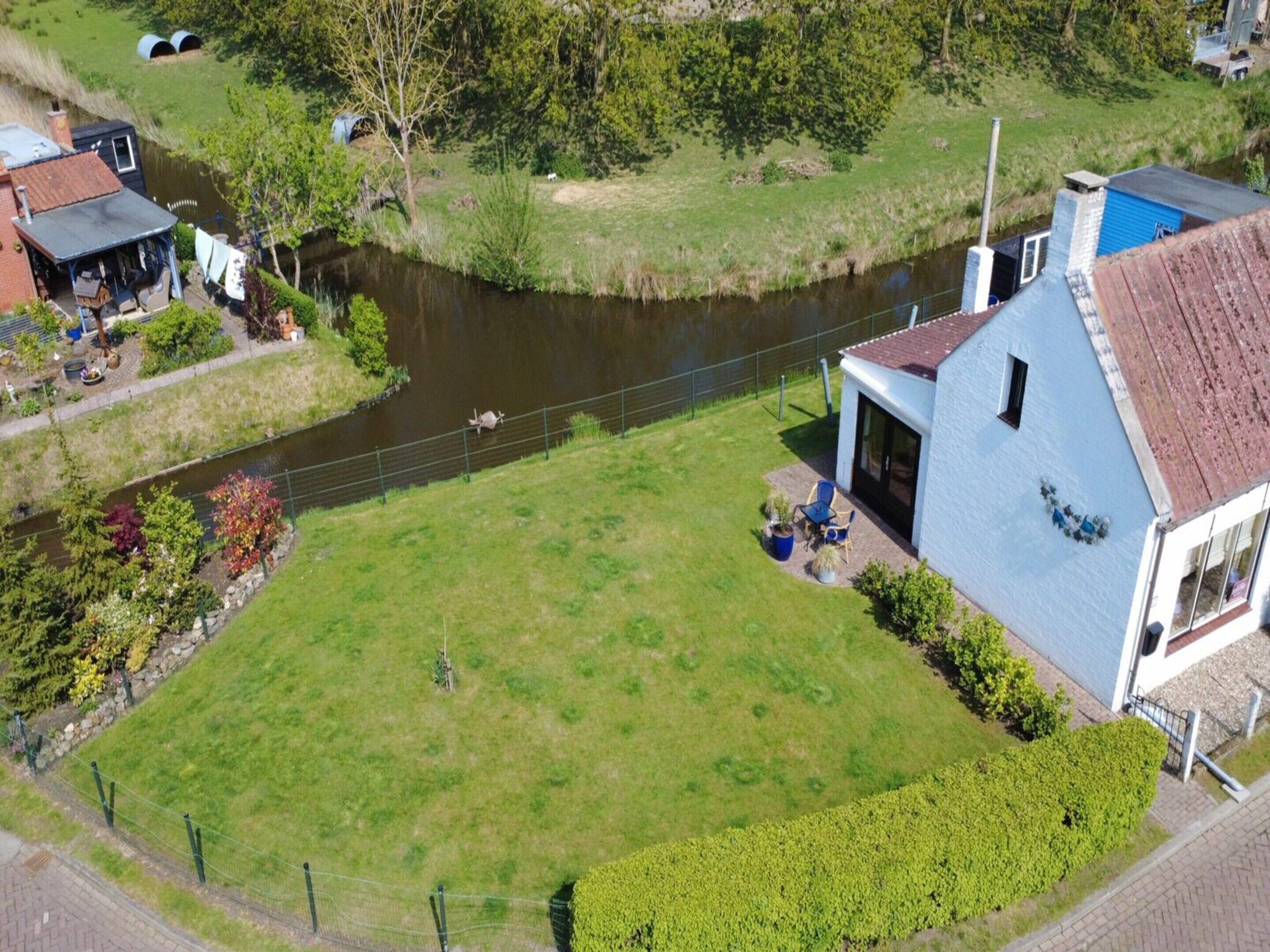 Una propiedad a orillas del río con césped, un muelle pequeño y un edificio azul de fachada blanca.