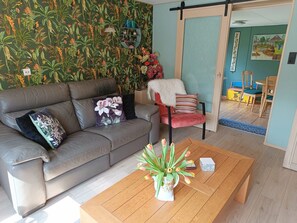 A living room with a sofa, a chair, a coffee table, and a wall with a tropical wallpaper. - Pet-friendly Zeeland Getaway (Schoondijke)