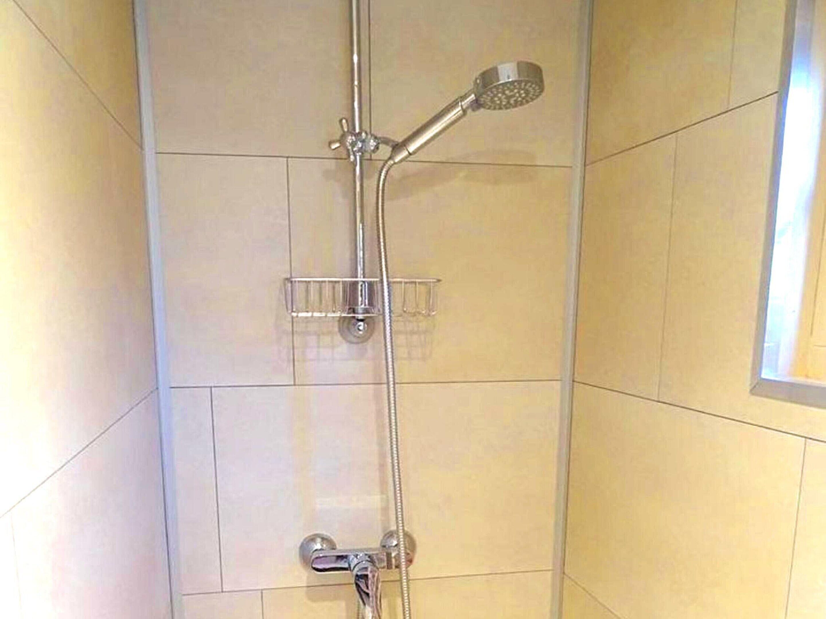 A shower with a handheld showerhead and a wall-mounted faucet.