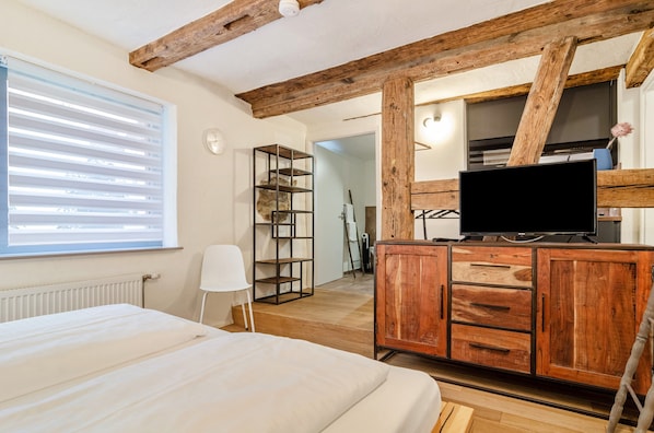 Une chambre avec un plafond en bois, un lit, une télévision, une armoire et une fenêtre avec des stores.