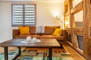 Uma sala de estar com sofá, mesa de centro, janela com persianas, abajur e lareira.