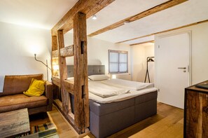 Um quarto com cama, estrutura de vigas de madeira, sofá e porta.